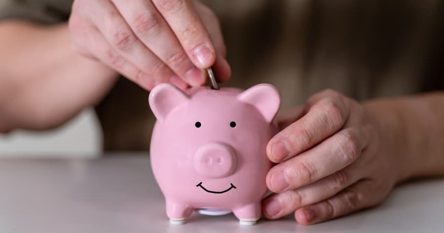 Manos depositando una moneda en una alcancía, programa de Subsidios